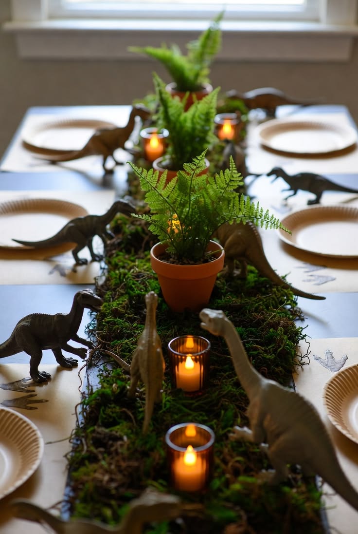 Green moss runner down the center of a table with small potted ferns, flickering tea lights, and toy dinosaurs walking among white plates.